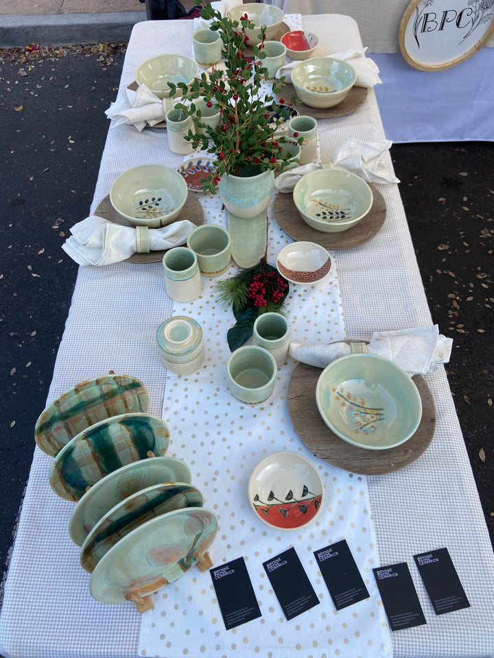 Ceramic pieces for a table setting indoor or outdoor. Plates, cups, bowls, napkin rings, vase, platter, and butter dish. Table setting with ceramics and linens. Tablescape with centerpiece. Light green, mint green, colorful, floral prints and solid colors